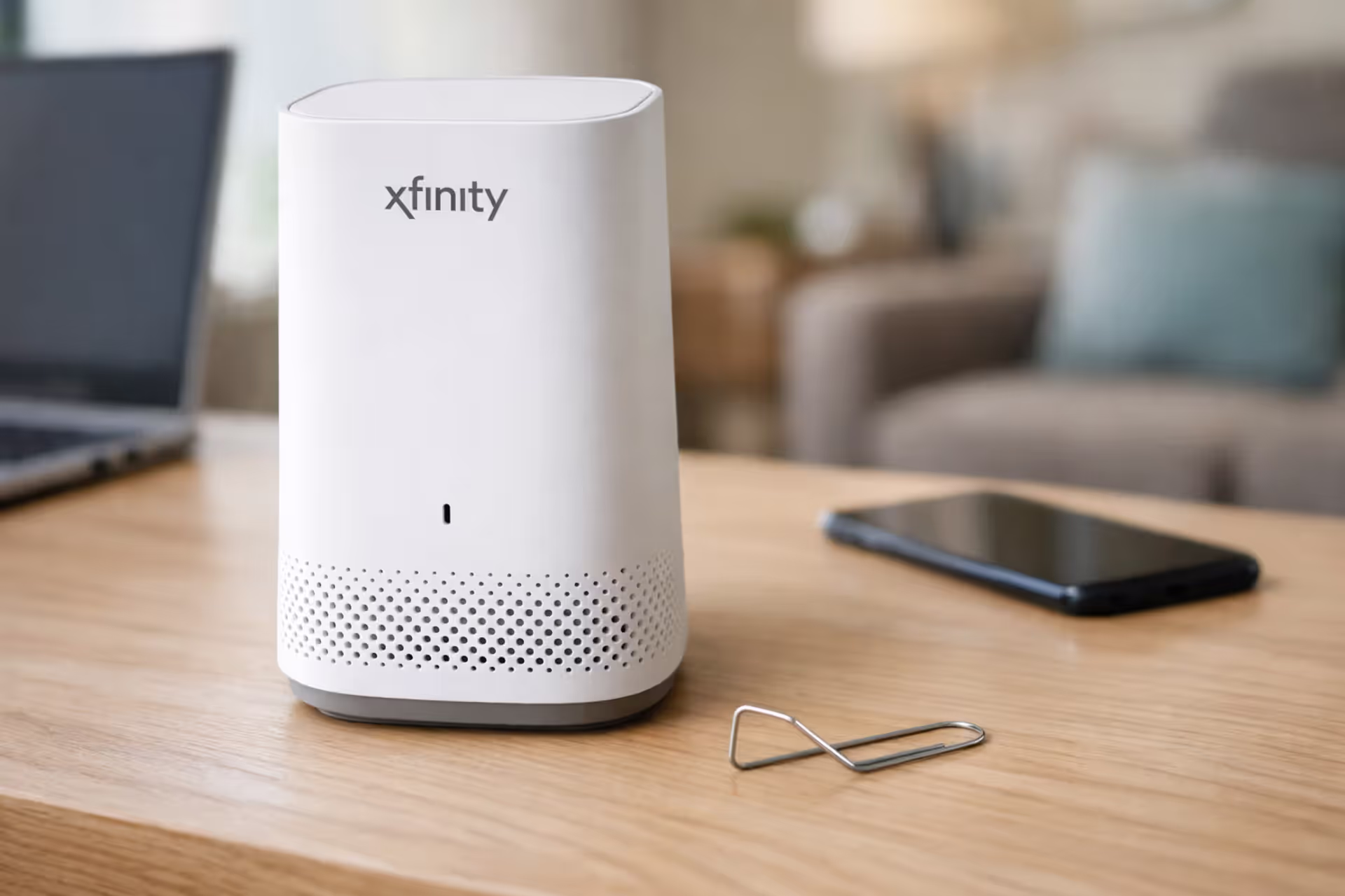 Xfinity Panoramic WiFi gateway on a desk with a paperclip near the reset button in a modern living room